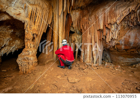 A speleologist with helmet and headlamp exploring a cave with rich stalactite and stalagmite A speleologist with helmet and headlamp exploring a cave with rich stalactite and stalagmite 113070955