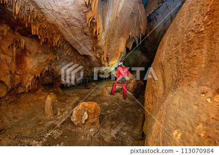 A speleologist with helmet and headlamp exploring a cave with rich stalactite and stalagmite 113070984