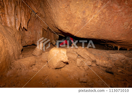 A speleologist with helmet and headlamp exploring a cave with rich stalactite and stalagmite A speleologist with helmet and headlamp exploring a cave with rich stalactite and stalagmite 113071010