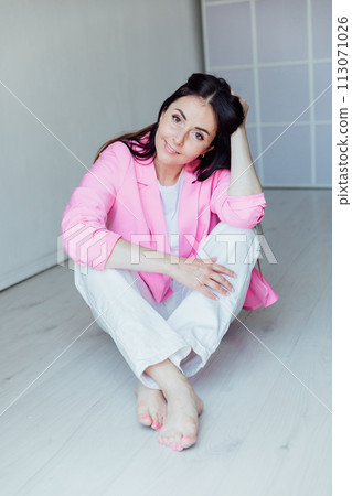 Beautiful fashionable woman sitting on the floor in pink jacket and white pants 113071026