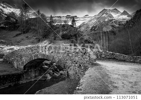 Sunset over the Pyrenees mountains, Circus of Gavarnie and the old stone bridge spanning the stream  113071051