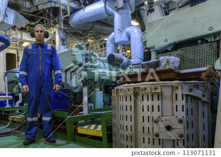 Marine Engineer in blue overall working in Engine room of ship. Work at sea. Motorman. 113071131