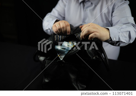 A business man was given a bribe of money dollars in a large bag on a black background. A businessman zips up a bag with a million dollars. Concept of bureaucracy, bribery. 113071401