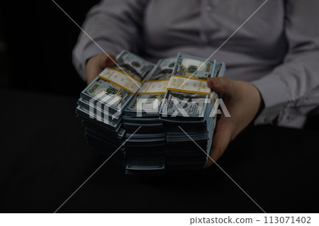 Close-up of hands sorting through stacks of dollars on a black background. A man shifts the day in packs on a black background close-up. Concept of wealth, money, savings. 113071402