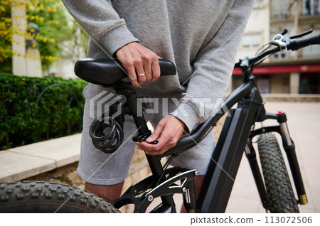 Close-up guy adjusting the height of new battery powered bike, electric bicycle before taking it out for the first ride. 113072506