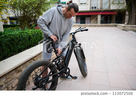 Caucasian young man cyclist adjusting a seat on electric bike. Bike sharing city service. Eco-friendly public transport 113072508
