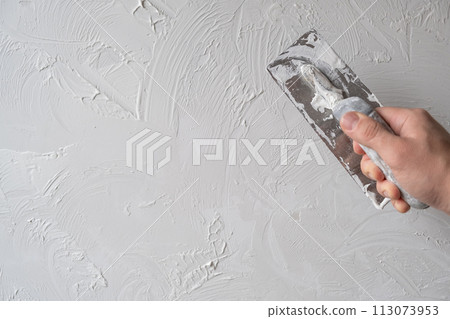 Applying decorative putty. White abstract texture of surface covered with putty. textured background of filler paste applied with putty knife in irregular dashes and strokes. Rough surface plaster 113073953