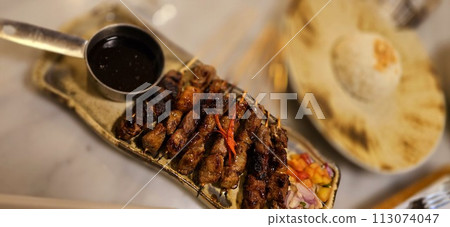 Homemade beef Satay marinated with spice and sweet soy sauce, coriander beef satay, served on plate with onion, chilli, soy sauce and tomato 113074047