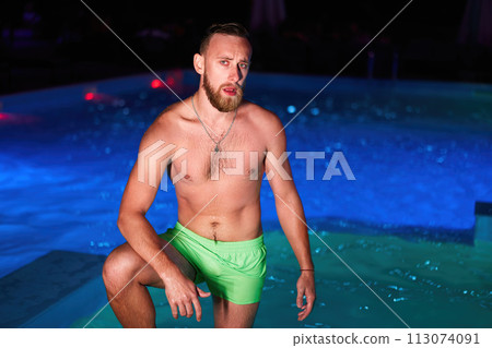 Seductive homosexual man celebrating gay pride with at night LGBTQ pool party in a private villa swimming pool. Bisexual male in swimwear posing on camera. Seductive homosexual man celebrating gay pride with at night LGBTQ pool party in a private villa swimming pool. Bisexual male in swimwear posing on camera. 113074091