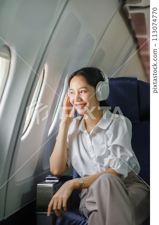 Asian woman sitting and using a smartphone in an airplane Listening to music next to the airplane seat window travel and technology concept Asian woman sitting and using a smartphone in an airplane Listening to music next to the airplane seat window travel and technology concept 113074770