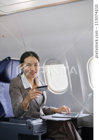 Asian female using laptop computer and holding credit card in airplane, Business traveling and technology concept. Asian female using laptop computer and holding credit card in airplane, Business traveling and technology concept. 113074810