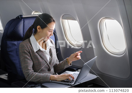 Asian female using laptop computer and holding credit card in airplane, Business traveling and technology concept. Asian female using laptop computer and holding credit card in airplane, Business traveling and technology concept. 113074820