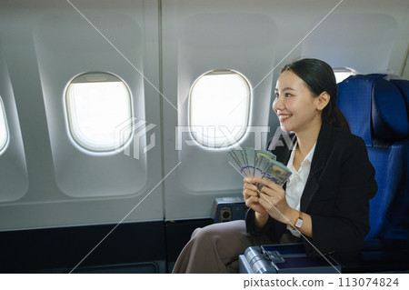 Asian attractive business woman passenger sitting on a plane and holding among of dollars. 113074824