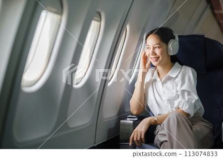 Asian woman sitting and using a smartphone in an airplane Listening to music next to the airplane seat window travel and technology concept Asian woman sitting and using a smartphone in an airplane Listening to music next to the airplane seat window travel and technology concept 113074833