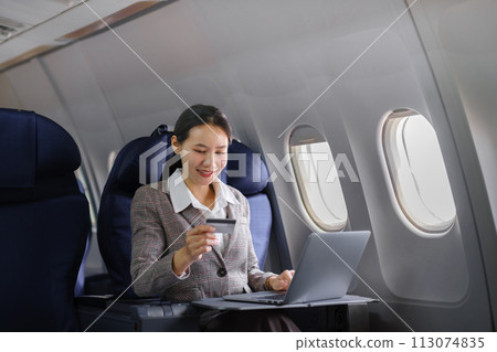 Asian female using laptop computer and holding credit card in airplane, Business traveling and technology concept. 113074835