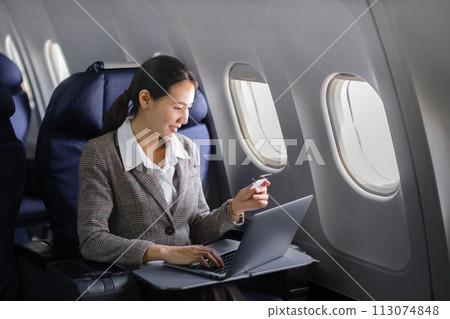 Asian female using laptop computer and holding credit card in airplane, Business traveling and technology concept. Asian female using laptop computer and holding credit card in airplane, Business traveling and technology concept. 113074848