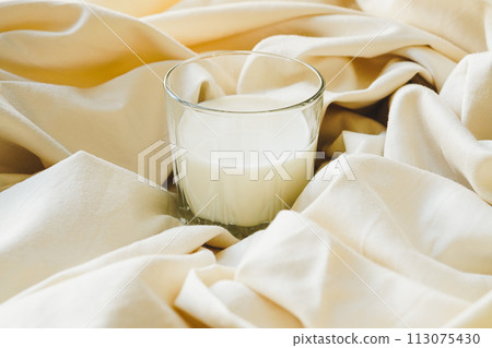 Glass filled with milk against white silk background 113075430