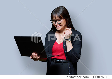Smiling business middle aged woman using laptop on gray background Smiling business middle aged woman using laptop on gray background 113076115