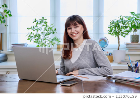 Young female college student studying at home using laptop, looking at camera Young female college student studying at home using laptop, looking at camera 113076159