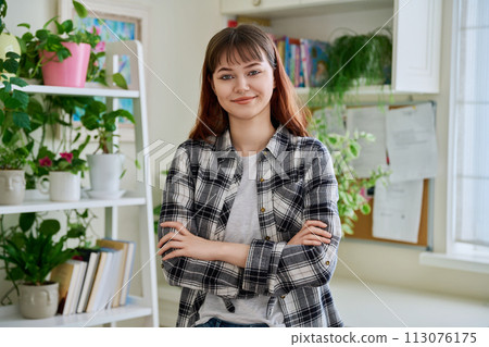 Portrait of smiling female teenager looking at camera with crossed arms in home 113076175