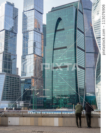 People on the background of skyscrapers. Modern architecture. Made of glass and concrete. Beautiful new skyscrapers. High-rise buildings in Moscow. Many windows. People on the background of skyscrapers. Modern architecture. Made of glass and concrete. Beautiful new skyscrapers. High-rise buildings in Moscow. Many windows. 113076906