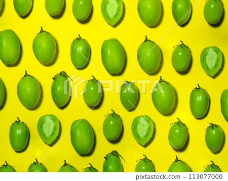 Green tomatoes on a yellow background. The concept of an unripe vegetable. Background from green vegetables. Salting product. 113077000