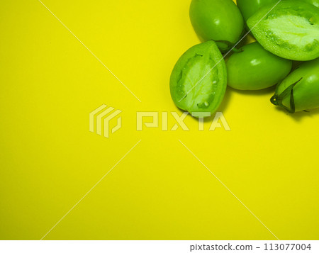 Green tomatoes on a yellow background. The concept of an unripe vegetable. Background from green vegetables.  Healthy food. Place for writing text 113077004