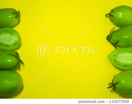 Green tomatoes on a yellow background. The concept of an unripe vegetable. Background from green vegetables. Healthy food. Place for writing text Green tomatoes on a yellow background. The concept of an unripe vegetable. Background from green vegetables. Healthy food. Place for writing text 113077009