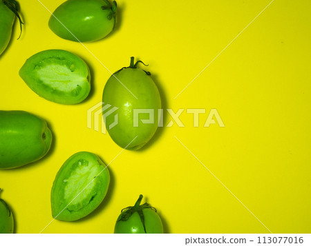 Green tomatoes on a yellow background. The concept of an unripe vegetable. Background from green vegetables. Salting product. Healthy food. Place for writing text. Tomatoes lady's fingers. Green tomatoes on a yellow background. The concept of an unripe vegetable. Background from green vegetables. Salting product. Healthy food. Place for writing text. Tomatoes lady's fingers. 113077016