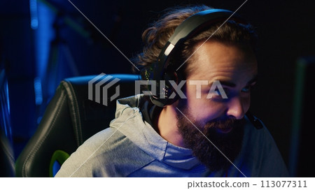 Esports player playing videogames in front of subscribers during livestream, providing knowledgeable commentary during gameplay. Zoom in on professional gamer streaming game in dark studio 113077311