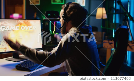 Angry gamer raging in frustration after losing level while playing spaceship videogame. Upset player furiously hitting table, getting flying spacecraft destroyed in game, receiving game over message 113077403