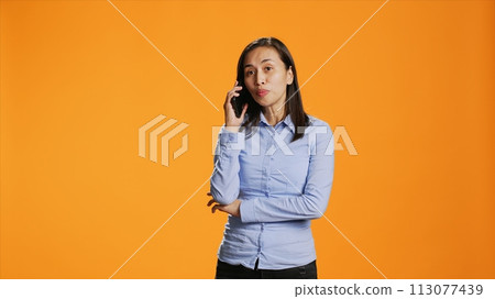 Relaxed person accepting calls in front of the lens interacting with friends on mobile telecoms connection. In the studio, asian girl answers smartphone for remote conversation, chatting. Relaxed person accepting calls in front of the lens interacting with friends on mobile telecoms connection. In the studio, asian girl answers smartphone for remote conversation, chatting. 113077439