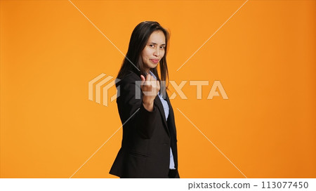 Proud business manager calling for someone in studio, doing hailing gesture with arm raised. Asian female model asking person to come here closer for a discussion against background. Proud business manager calling for someone in studio, doing hailing gesture with arm raised. Asian female model asking person to come here closer for a discussion against background. 113077450