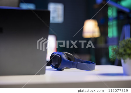 Selective focus on wireless headphones placed on a table near digital laptop. Image showing electronic devices kept on a desk for an individual to use. 113077819