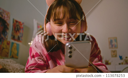 Teenage girl talks by video call using phone lying on the bed in cozy bedroom 113078253