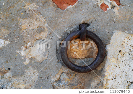 Clappers on an ancient stone wall. Old iron circle to hang boats 113079440