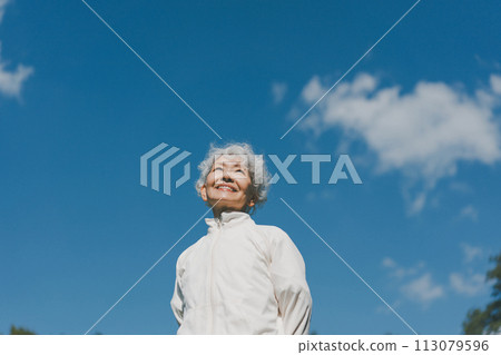 A woman in her 60s in the park looks at the sky 113079596