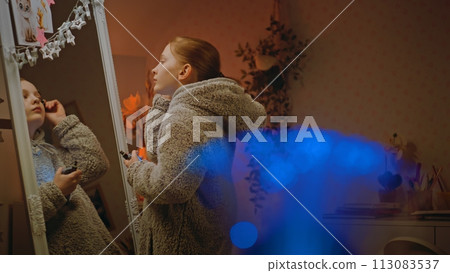 Teenage girl does eyebrows makeup standing and looking in the mirror in bedroom Teenage girl does eyebrows makeup standing and looking in the mirror in bedroom 113083537