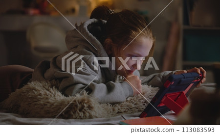 Young girl lies on bed at home, surfs the Internet using tablet computer Young girl lies on bed at home, surfs the Internet using tablet computer 113083593
