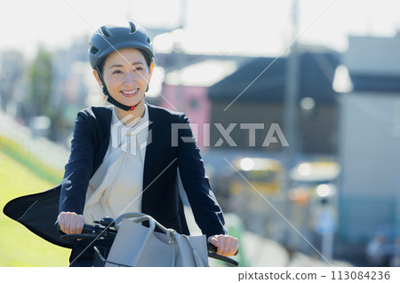 Middle-aged woman commuting to work on a bicycle Middle-aged woman commuting to work on a bicycle 113084236