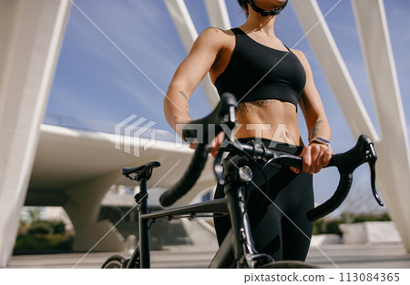 Close up of female cyclist standing with her bike before cycling Close up of female cyclist standing with her bike before cycling 113084365