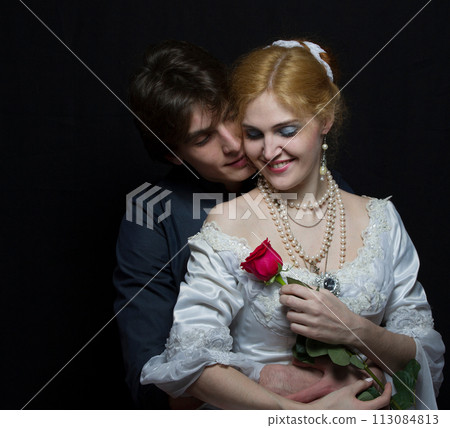 Beautiful couple in retro style. A man hugs a woman. Girl in a white dress with a red rose on a background of a man. 113084813