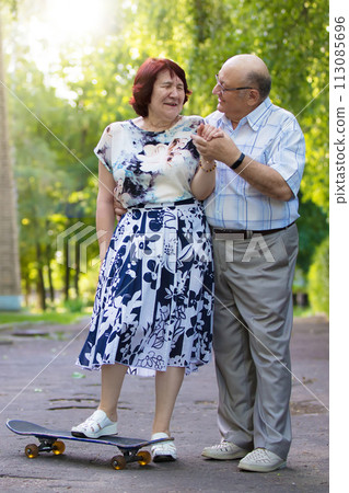Happy elderly couple with a skateboard. Handsome man and woman senior citizens. Husband and wife of old age for a walk in the city. 113085696