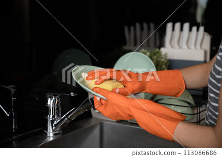 Close up woman protective gloves washing dishes with sponge in the kitchen sink Close up woman protective gloves washing dishes with sponge in the kitchen sink 113086686