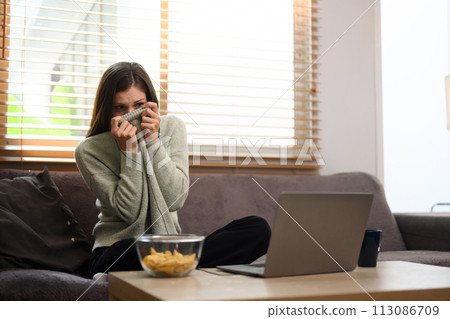 Scared young woman watching a horror movie at home. Entertainment and hobby concept 113086709