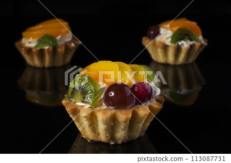 cake basket with kiwi fruit peach gooseberries close-up on a black background 113087731