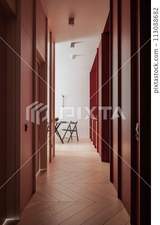 a long hallway with red walls and wooden floors leading to a room with a table and chairs 113088682