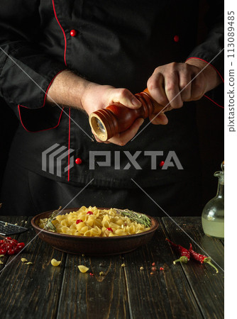 The chef adds hot peppers to a plate of pasta. Working environment on the kitchen table in the cook room. Delicious pasta with vegetables for lunch 113089485