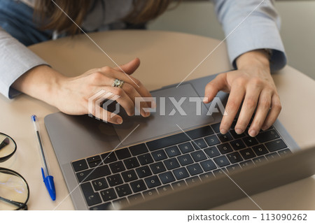 Close-up of the hands of a corporate woman dressed in a light blue formal shirt typing on her laptop 113090262