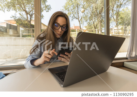 Business woman in light blue shirt and glasses working with her phone and laptop in the hotel 113090295